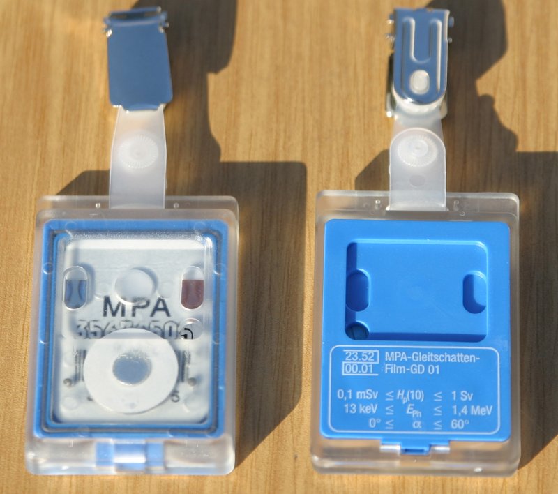 A film dosimeter radiation monitoring badge worn by radiologic technologists to measure occupational radiation dose, reported in mSv or mrem